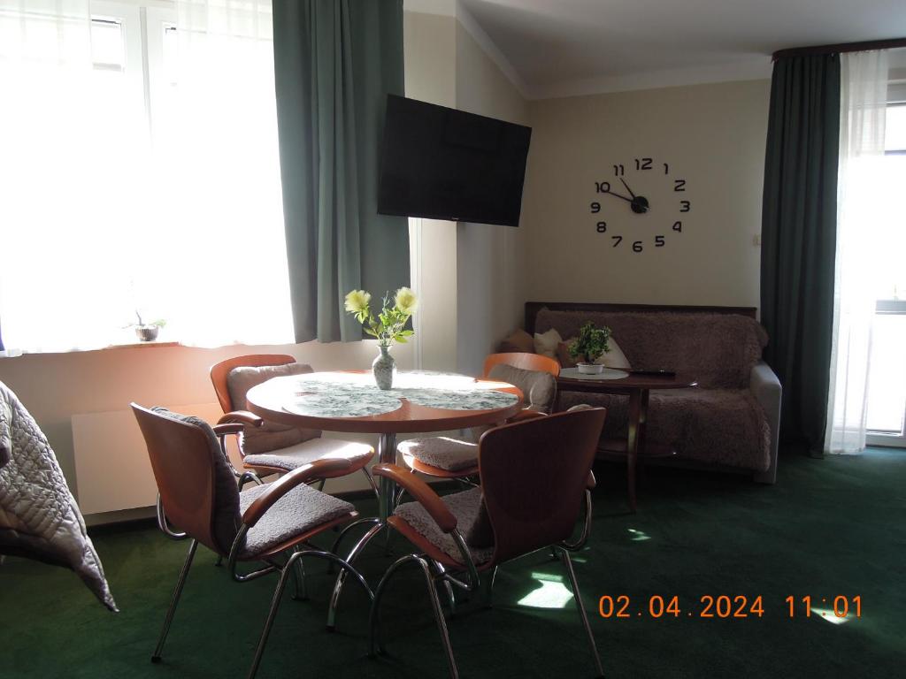 salon ze stołem, krzesłami i zegarem w obiekcie Rodzinny, słoneczny apartament w dzielnicy uzdrowiskowej, blisko plaży w Kołobrzegu