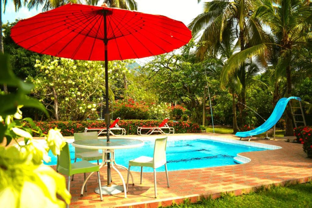 einen Tisch mit einem roten Regenschirm neben einem Pool in der Unterkunft Villas Mamilú. entrada y salida cien por ciento flexible in Santa Fe de Antioquia