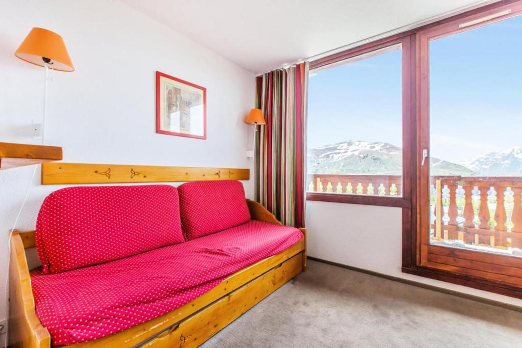 Cette chambre dispose d'un canapé rouge et d'une grande fenêtre. dans l'établissement Résidence Les Mélèzes - maeva Home - 2 pièces 6 pers Confort MAE-3394, à Huez