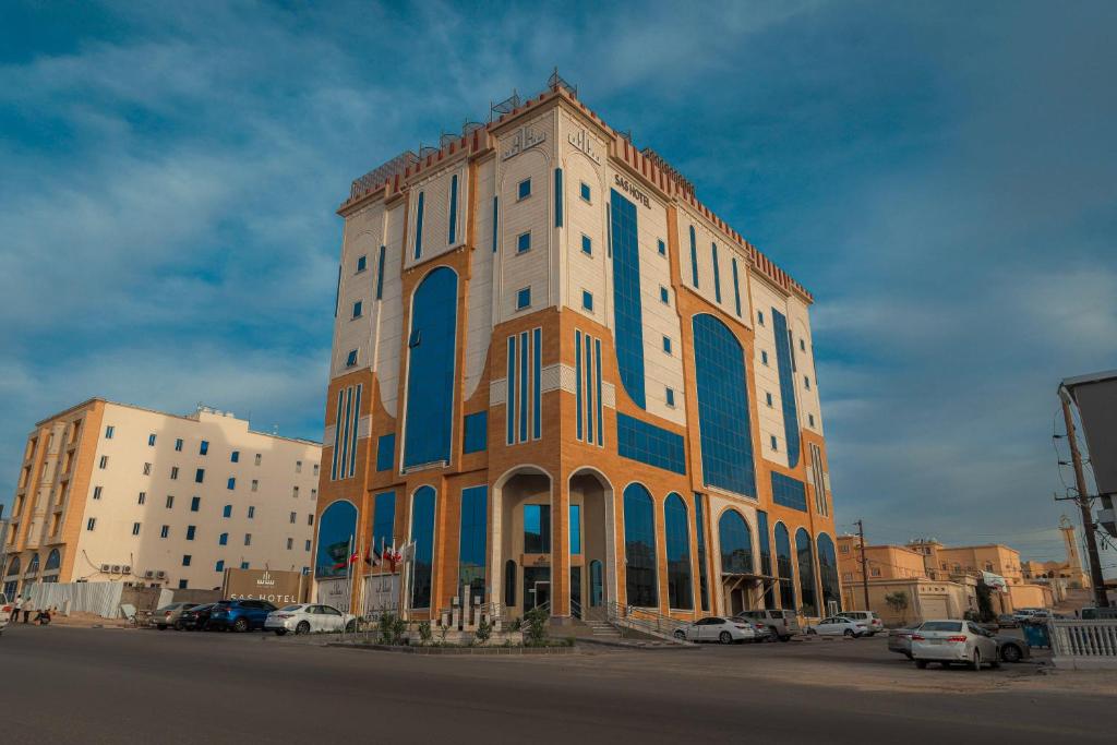 een oranje en blauw gebouw met auto's geparkeerd op een parkeerplaats bij فندق ساس - SAS Hotel in Hafr Al Baten