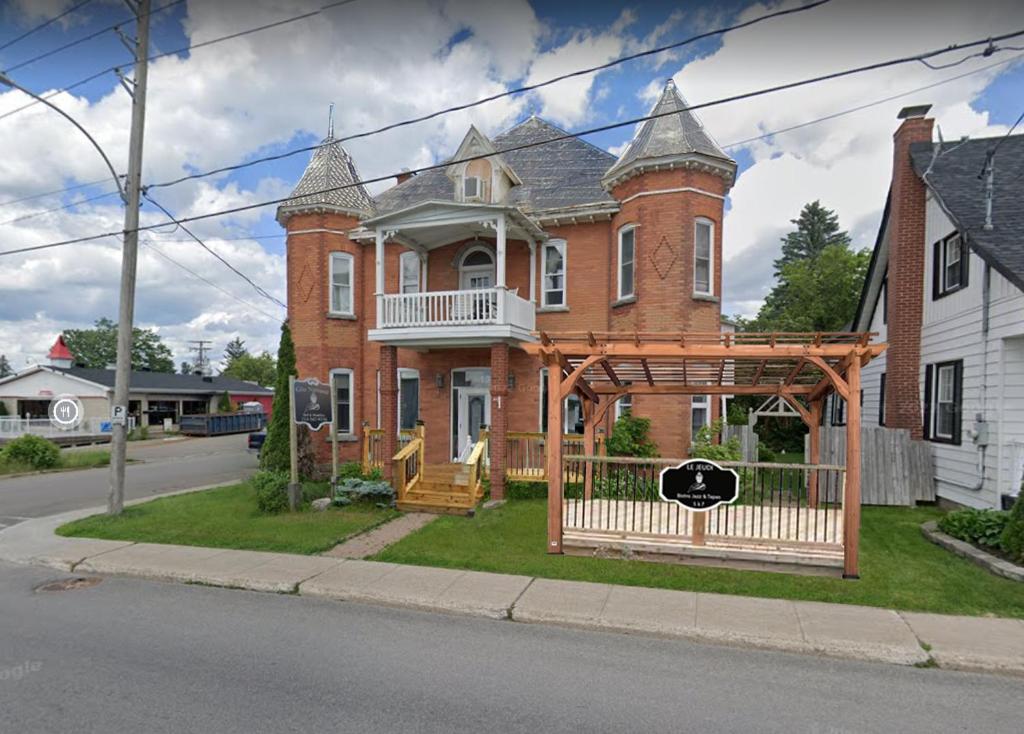 a large red brick house with a wooden gate at AUBERGE et BISTRO NAMASTÉ in Lachute