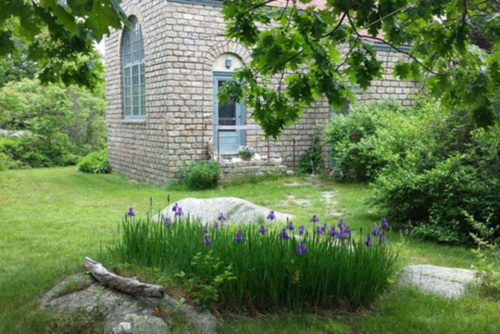 a brick house with purple flowers in the yard at Great Ledges Studio in Rockport
