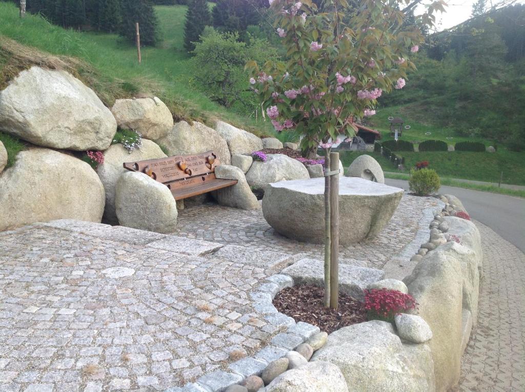 a park bench next to a tree and rocks at Holzbildhauerei Kammerer in Triberg