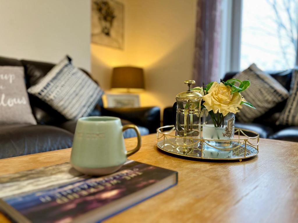 una mesa con una taza de café y un libro y flores en Cosy Apartment Glasgow Airport, en Paisley