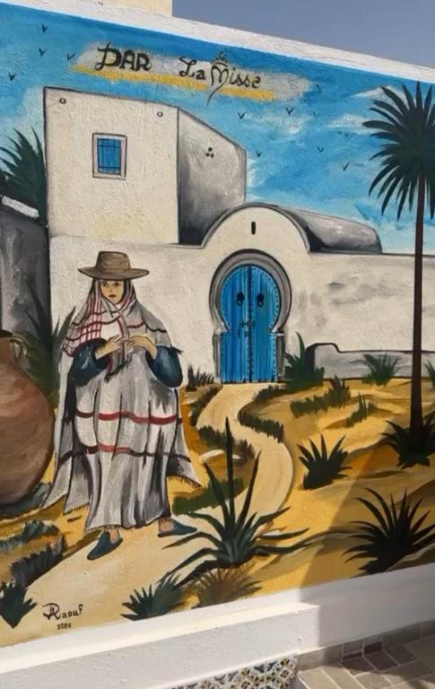 a painting of a woman in front of a building with a blue door at Dar Lamis in Houmt Souk