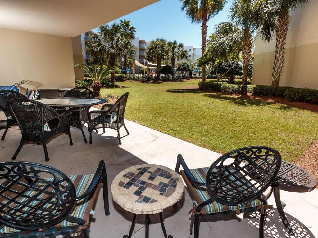 a patio with tables and chairs and a lawn with palm trees at Waterscape C206 Ground Floor in Fort Walton Beach