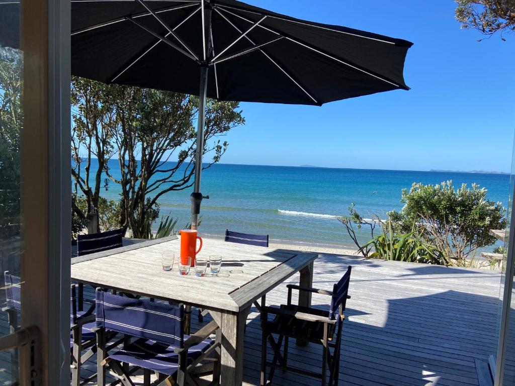 a table with chairs and an umbrella on the beach at Bliss on the Beach - Whangapoua in Whangapoua