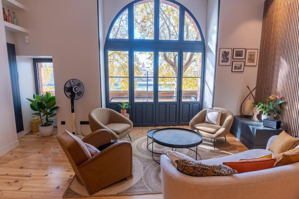 d'un salon avec des chaises, une table et une grande fenêtre. dans l'établissement Le Lombard : Panorama sur la Garonne, à Toulouse