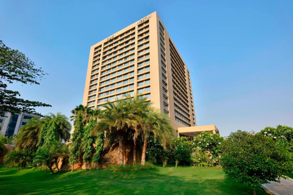 a tall building with palm trees in front of it at The Westin Hyderabad Mindspace in Hyderabad
