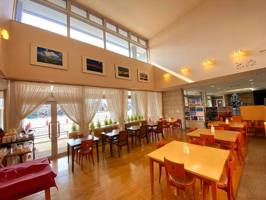 un restaurante con mesas y sillas de madera y ventanas en Hotel Lavenir, en Biei