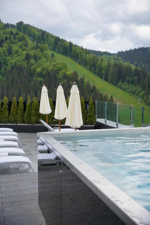 a pool with chairs and umbrellas next to a mountain at Mountain Residence Apartments & Chalet in Bukovel