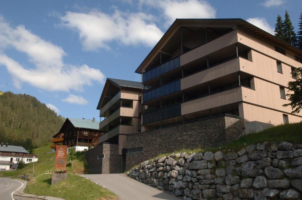 - un bâtiment sur une colline à côté d'un mur de pierre dans l'établissement Aparthotel Alpinresort Damüls, à Damüls