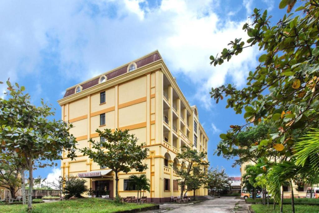 een geel gebouw met bomen ervoor bij Cửa Đại Beach Hotel in Hội An