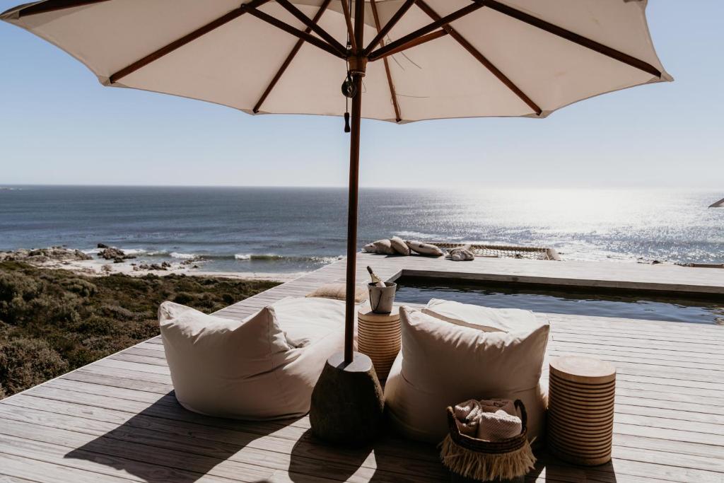 a table with pillows and an umbrella next to the ocean at Pure Sea Boutique Lodge in Gansbaai