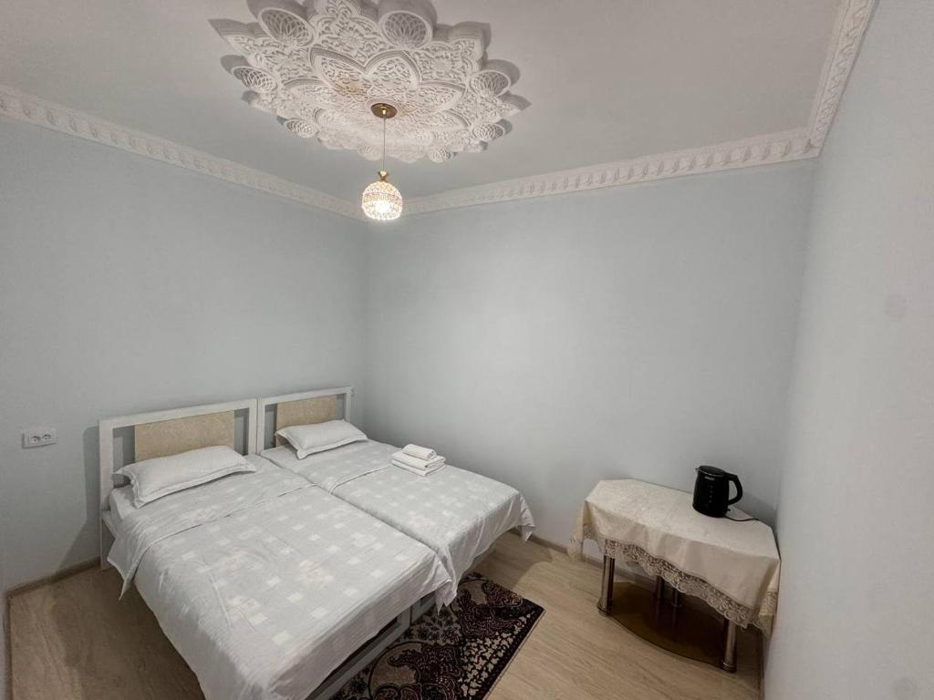 Dieses weiße Zimmer verfügt über 2 Betten und einen Kronleuchter. in der Unterkunft Boulevard Architectural Hotel Wifi 100 MBS in Buxoro