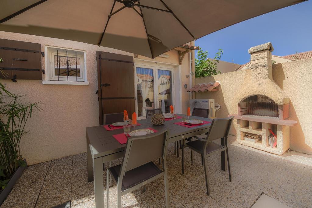 une table avec des chaises et un parasol sur une terrasse dans l'établissement La Barque, au Barcarès
