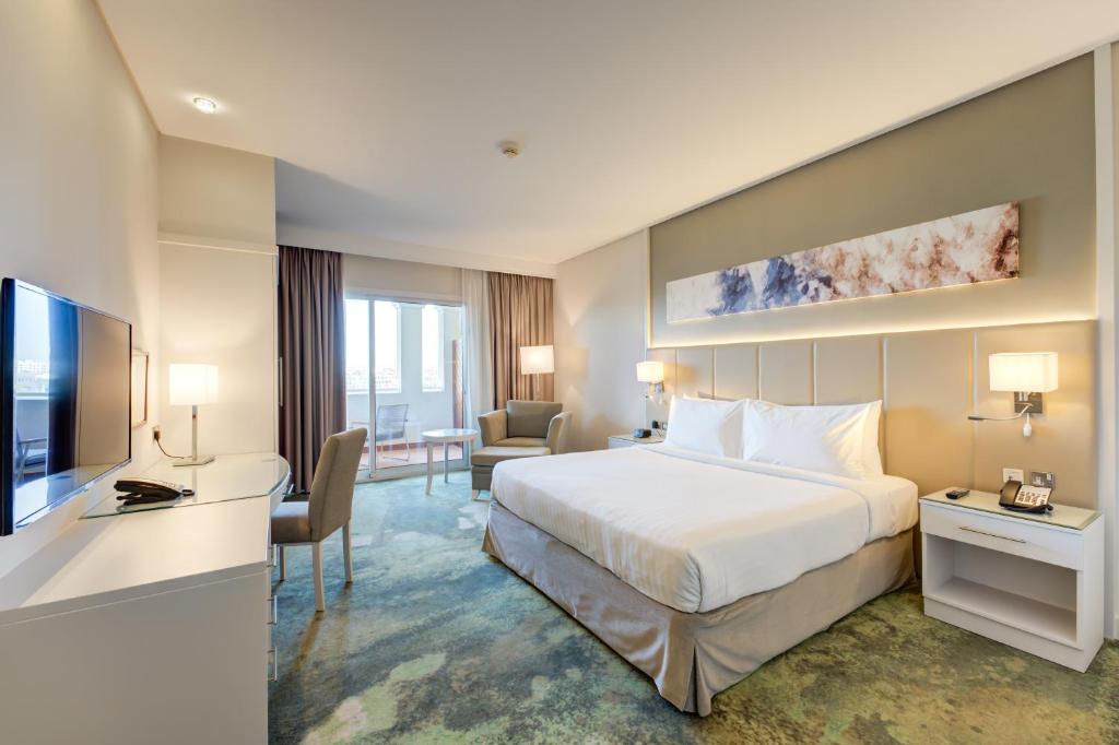 a hotel room with a bed and a desk and a television at Copthorne Lakeview Hotel Dubai, Green Community in Dubai