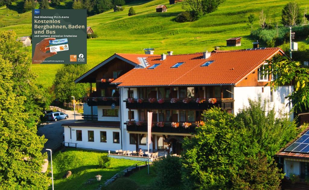 een groot huis met een rood dak en een heuvel bij Alpenhotel Sonneck - mit Bergbahnticket in Bad Hindelang