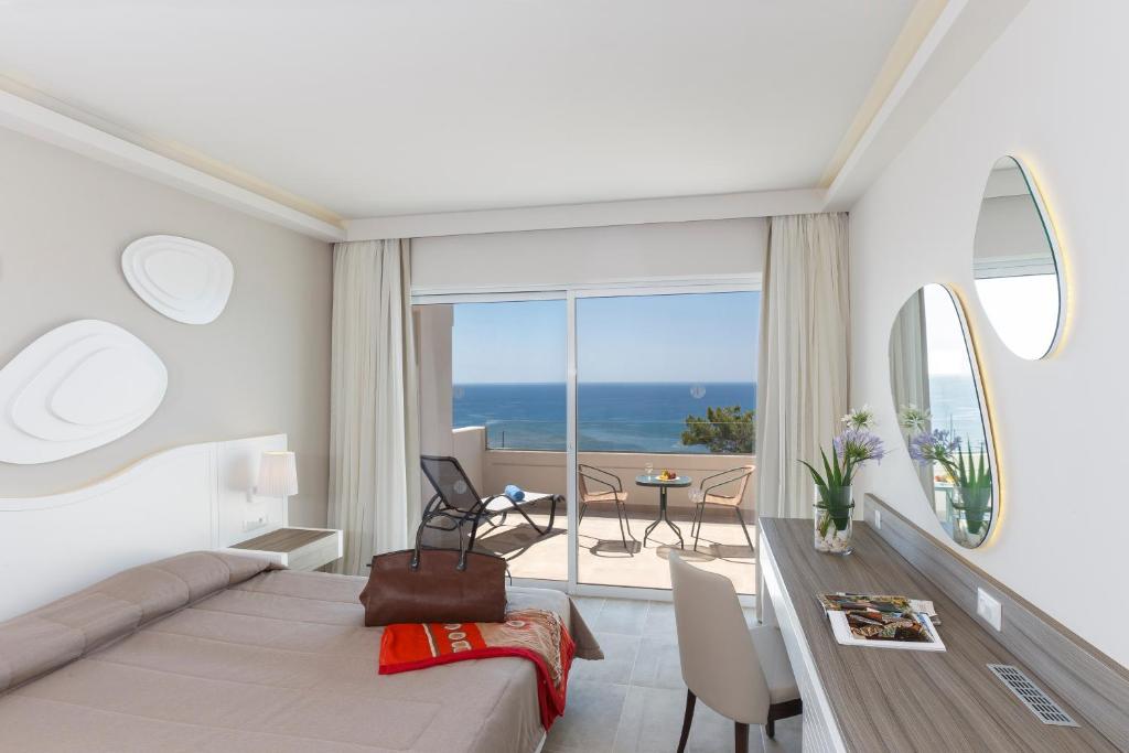 a bedroom with a bed and a dining room with a view at Rodos Princess Beach Hotel in Kiotari