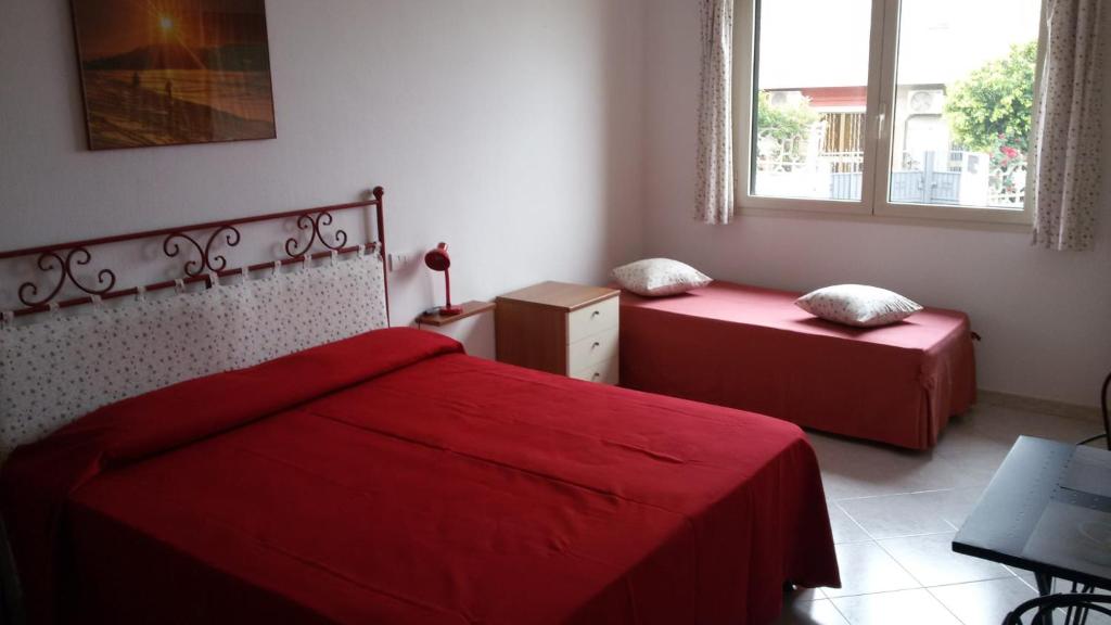 a bedroom with two red beds and a window at Ca'Mea in Villasimius