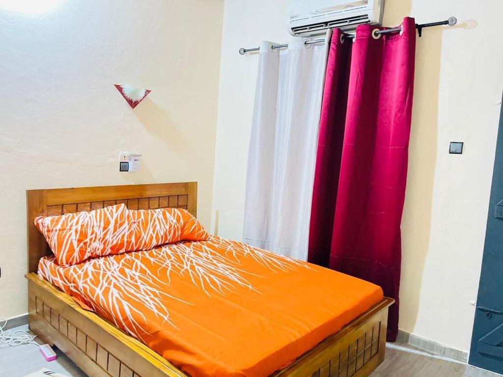 a bed with an orange comforter and a red curtain at Guest Bakhita in Abomey-Calavi