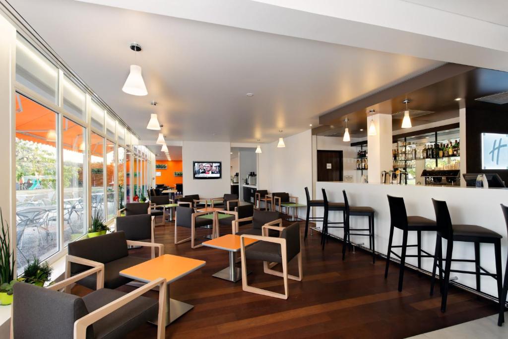 ein Restaurant mit Tischen und Stühlen und eine Bar in der Unterkunft Holiday Inn Express Strasbourg - Sud, an IHG Hotel in Geispolsheim