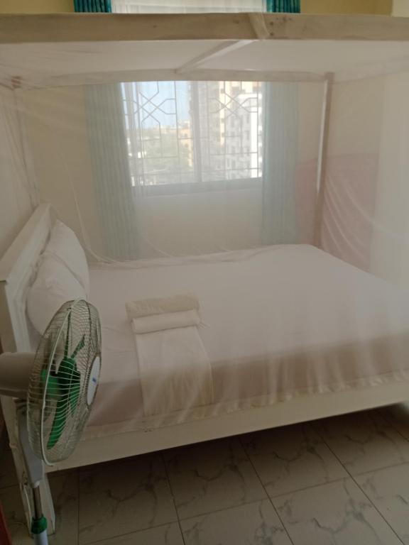 a white bed with a fan and a window at Home away from home Next to Sky Louge Bamburi in Mombasa