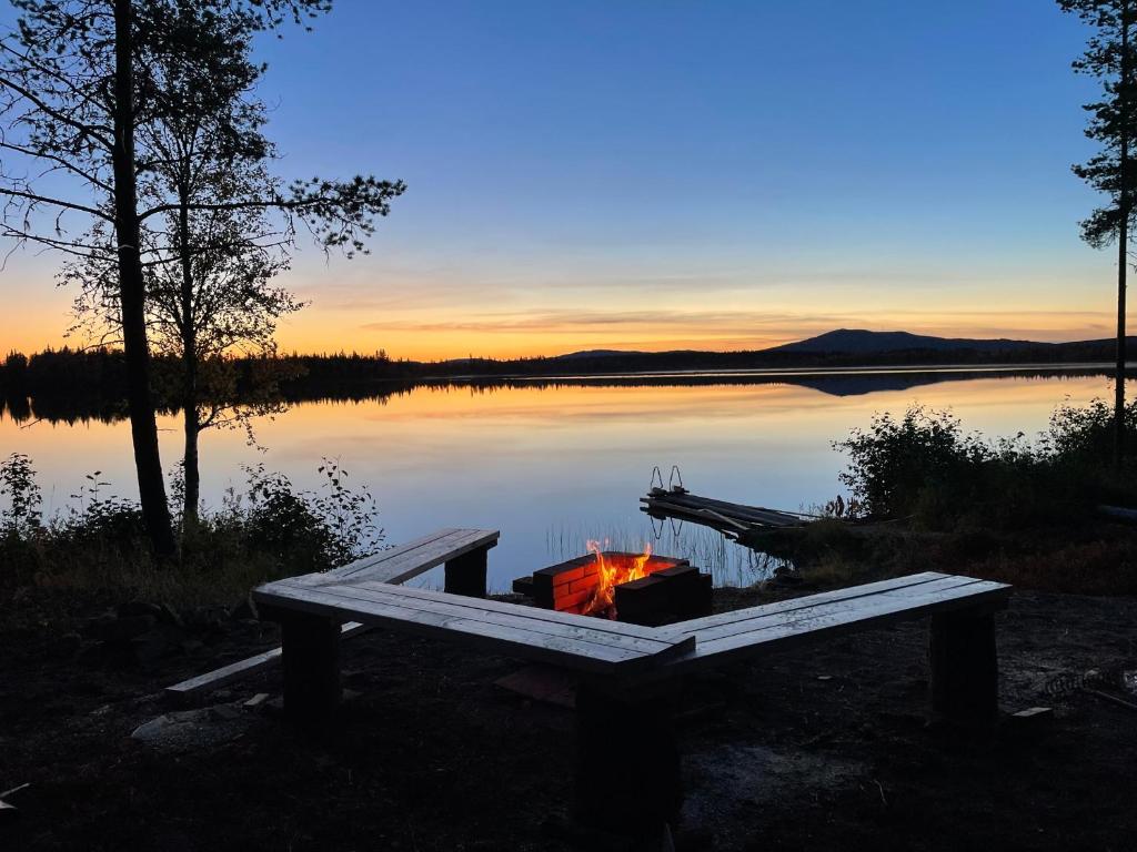 a fire pit next to a lake at sunset at Kenttäpirtti in Kittilä