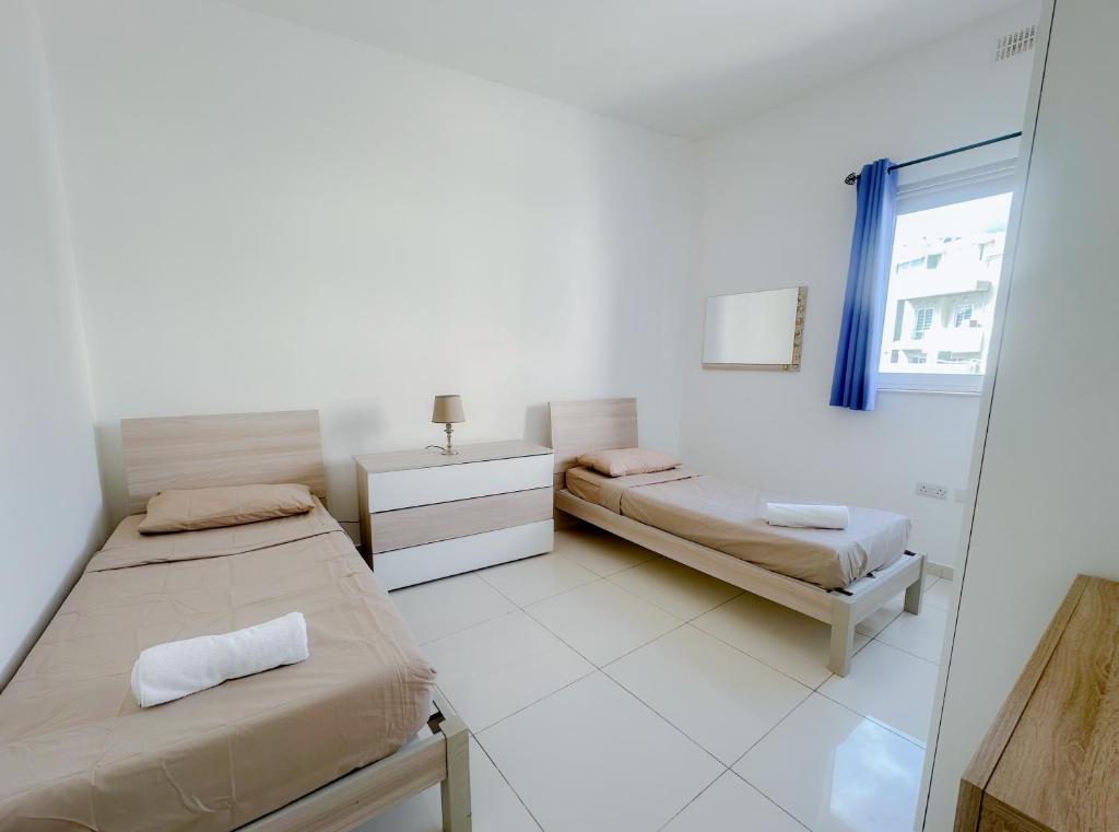 um quarto branco com 2 camas e um espelho em Lovely flat close to St julians with 6 beds in 3 rooms for 8 people em Is-Swieqi