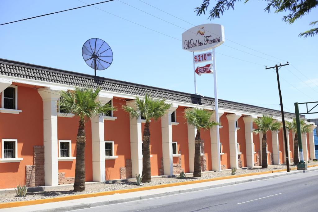 a red building with palm trees in front of it at Motel Las Fuentes in Mexicali