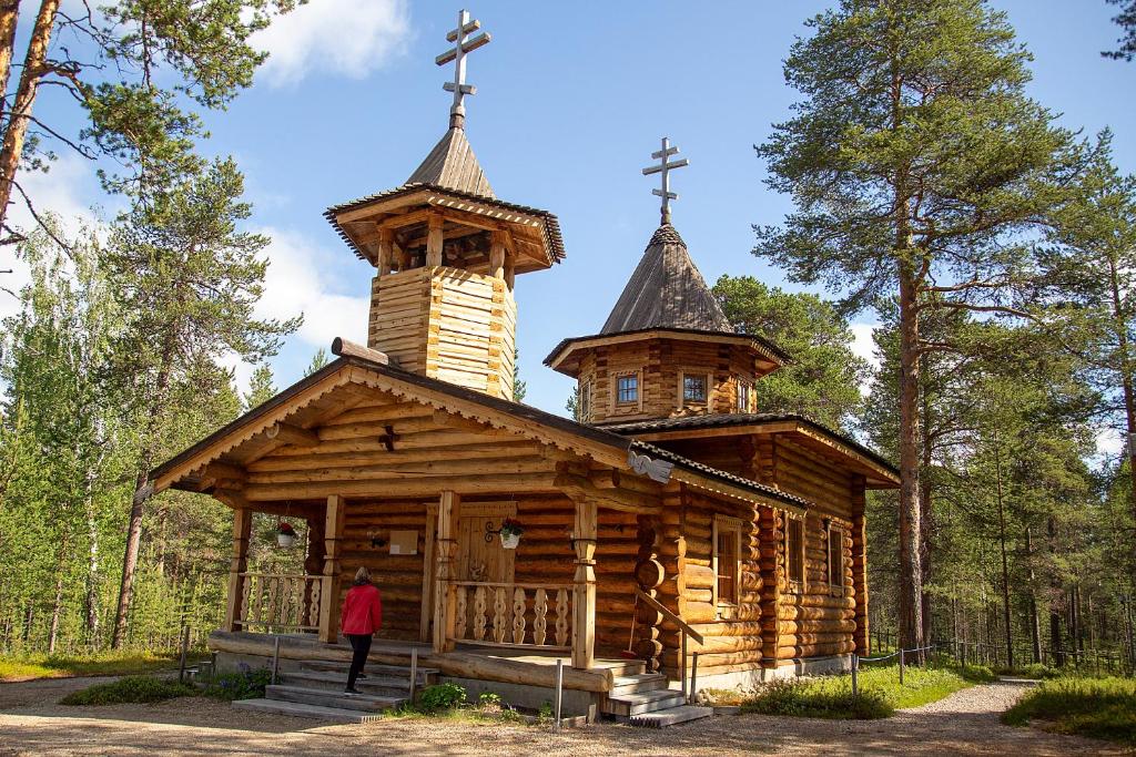 a small wooden church with a steeple and a person standing in front at Wilderness Hotel Nellim & Igloos in Inari