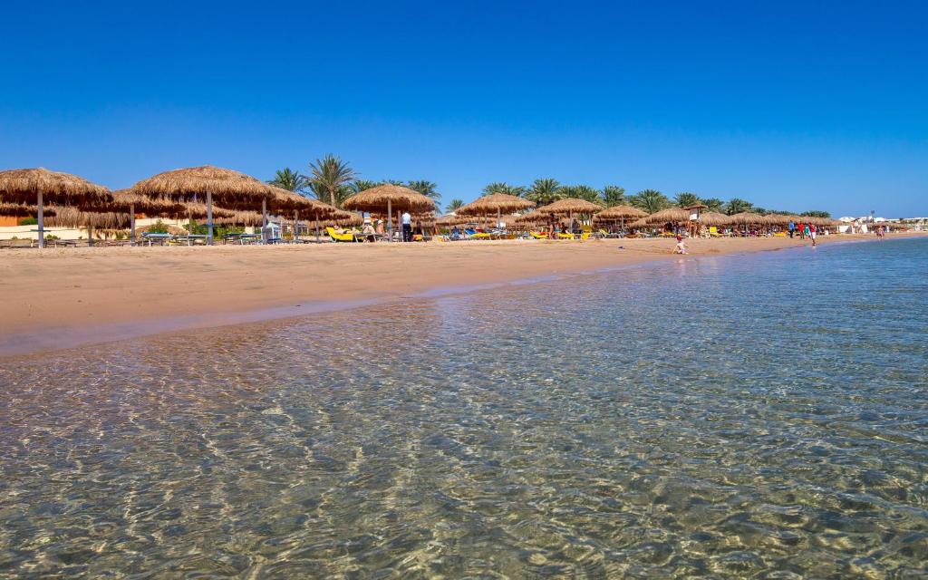 een strand met een aantal rieten parasols en het water bij Caribbean World Resort Soma Bay in Hurghada