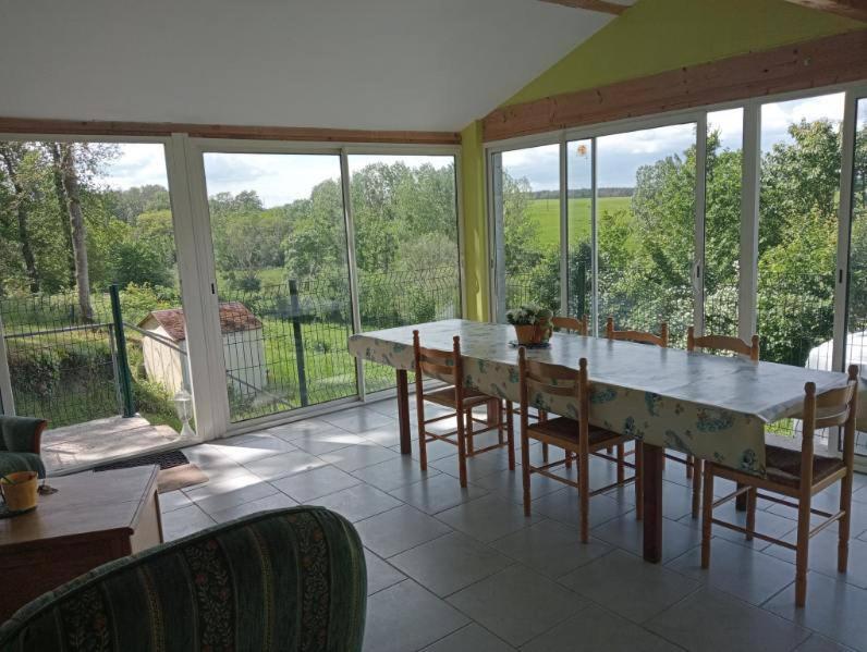 a dining room with a table and chairs and windows at Maison de campagne in Le Lude