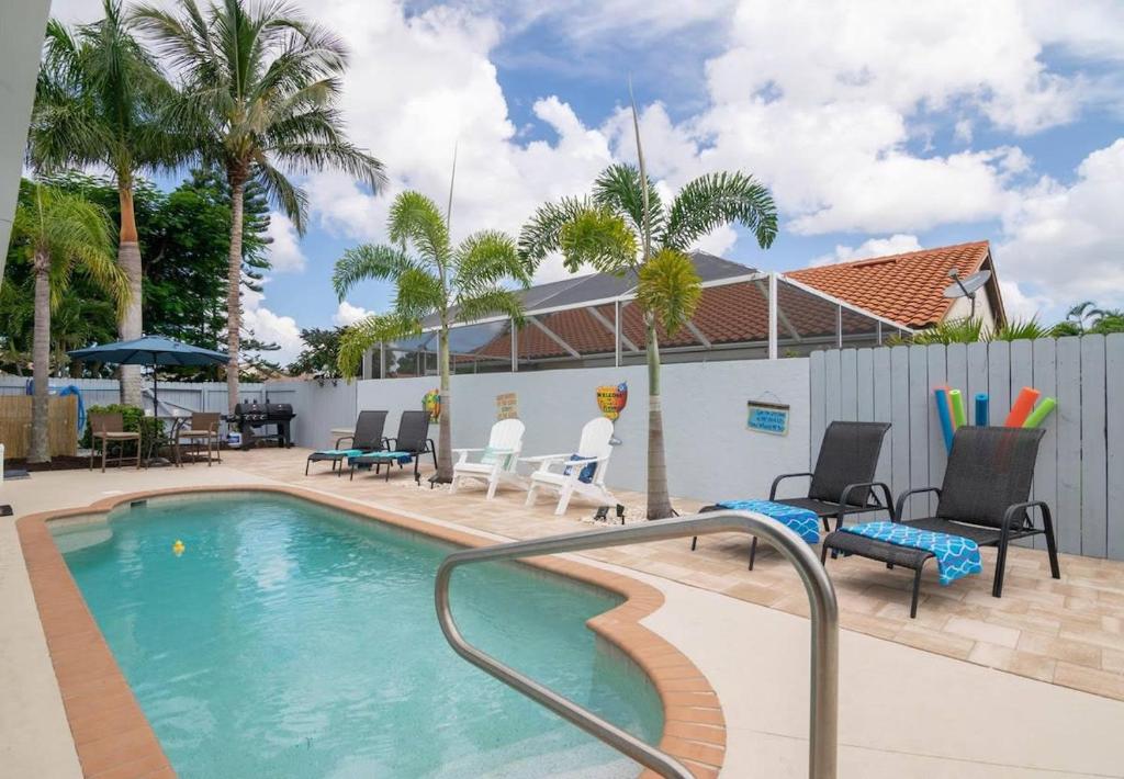 a swimming pool with chairs and a fence and palm trees at Charming Heated Pool Home - 3 miles to the Beach, Pet and Family Friendly -Available Year Round! in Bonita Springs