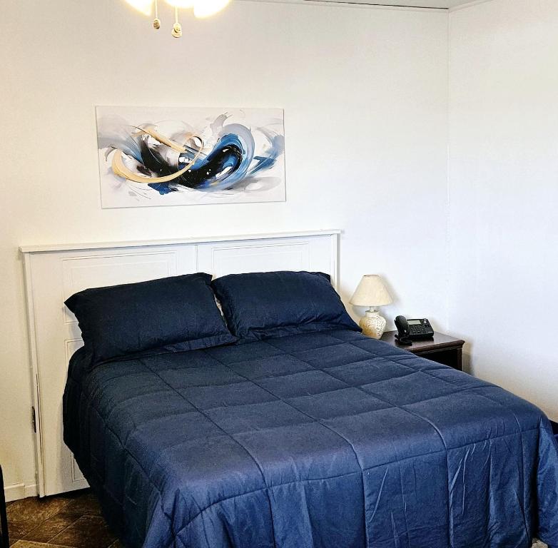 Un dormitorio con una cama azul y una pintura en la pared en Motel Au Soleil couchant, en Rimouski