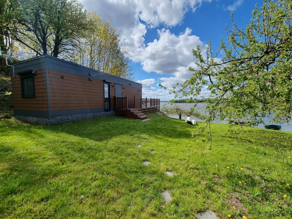 a small cabin in the grass next to a lake at GARDENIA RAJGRÓD in Rajgród