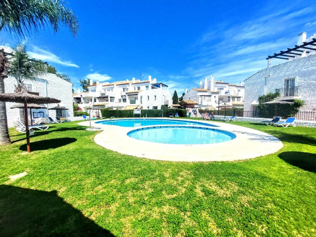 a swimming pool in the middle of a lawn with buildings at EL PARAISO GOLF Y PLAYA in Estepona