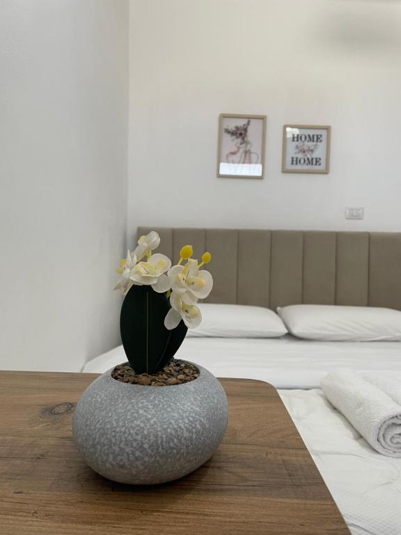 a vase with flowers on a table in front of a bed at Rent rooms Loren in Vlorë