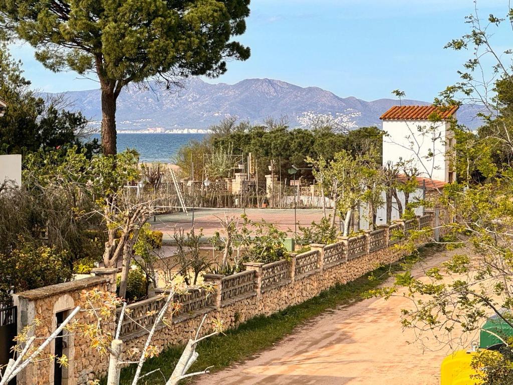 a garden with a stone wall and a tree and water at Villa Mercè Empúries in Sant Martí d’Empúries