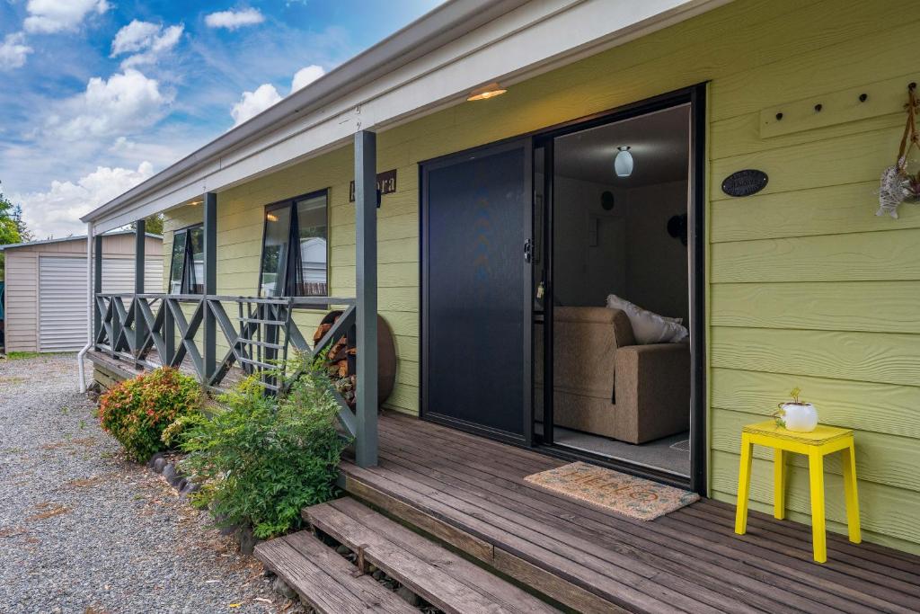 una veranda anteriore di una casa verde con sgabello giallo di The Yellow Cottage - Turangi Holiday Home a Turangi