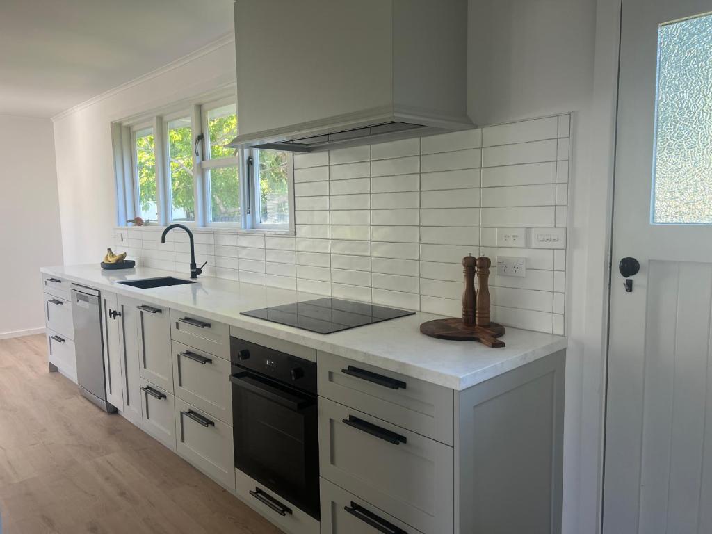 a white kitchen with a sink and a stove at Village Cottage in Havelock North