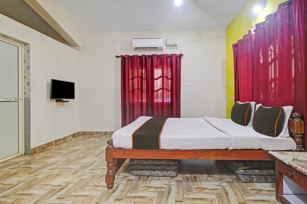 een slaapkamer met een bed met rode gordijnen en een televisie bij Ferns Guest House in Calangute