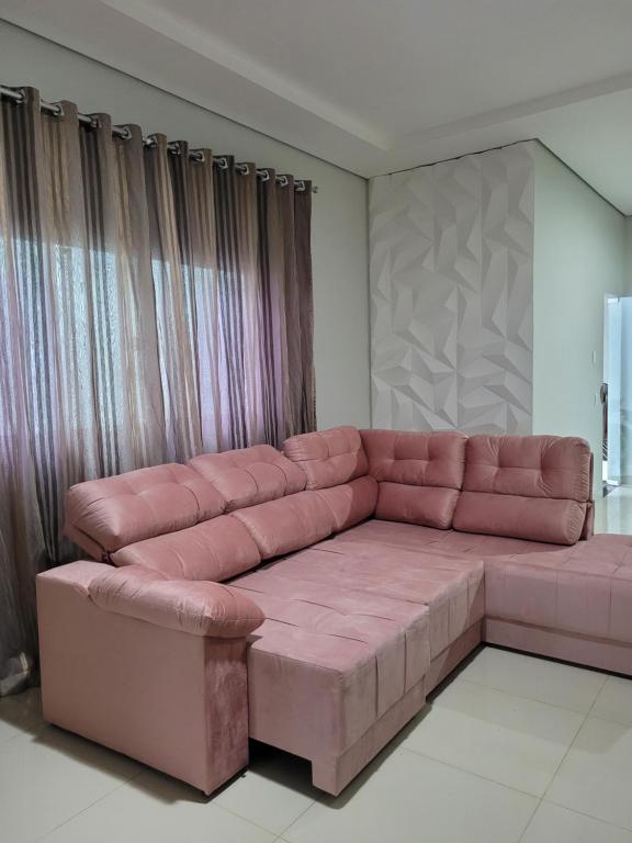 Sofá rosa en la sala de estar con cortinas en Casa agradável com área gourmet, en Ji-Paraná
