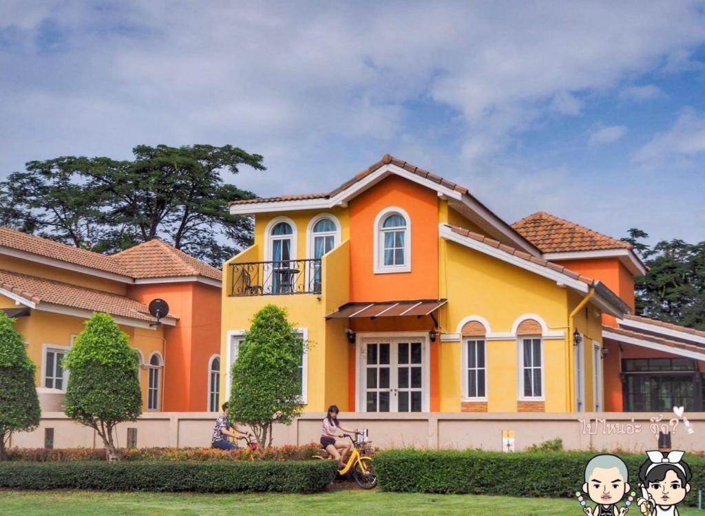 una casa amarilla y naranja con una persona en una motocicleta en Demu Plus Pool villa @Marino Khaoyai, en Nong Nam Daeng