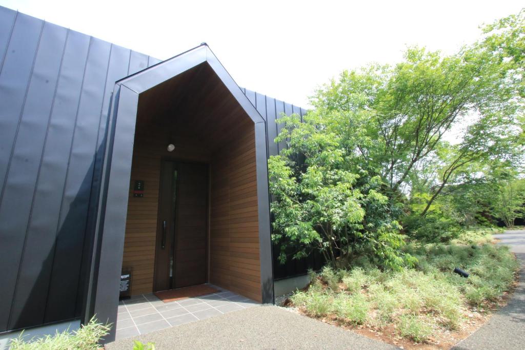 ein schwarzes Gebäude mit einer Holztür und einem Busch in der Unterkunft 御宿 白金の森 in Kikuchi