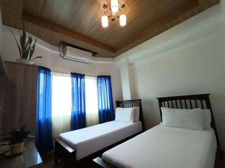 2 camas sentadas junto a una ventana con cortinas azules en Sillero Painting Gallery and Hostel en Dumaguete