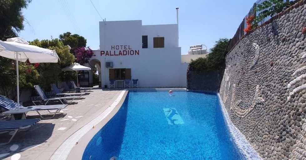 a swimming pool next to a building with chairs at Hotel Palladion in Karterados