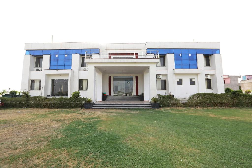 a large white building with blue windows and a yard at OYO Diamond Resort in Alwar
