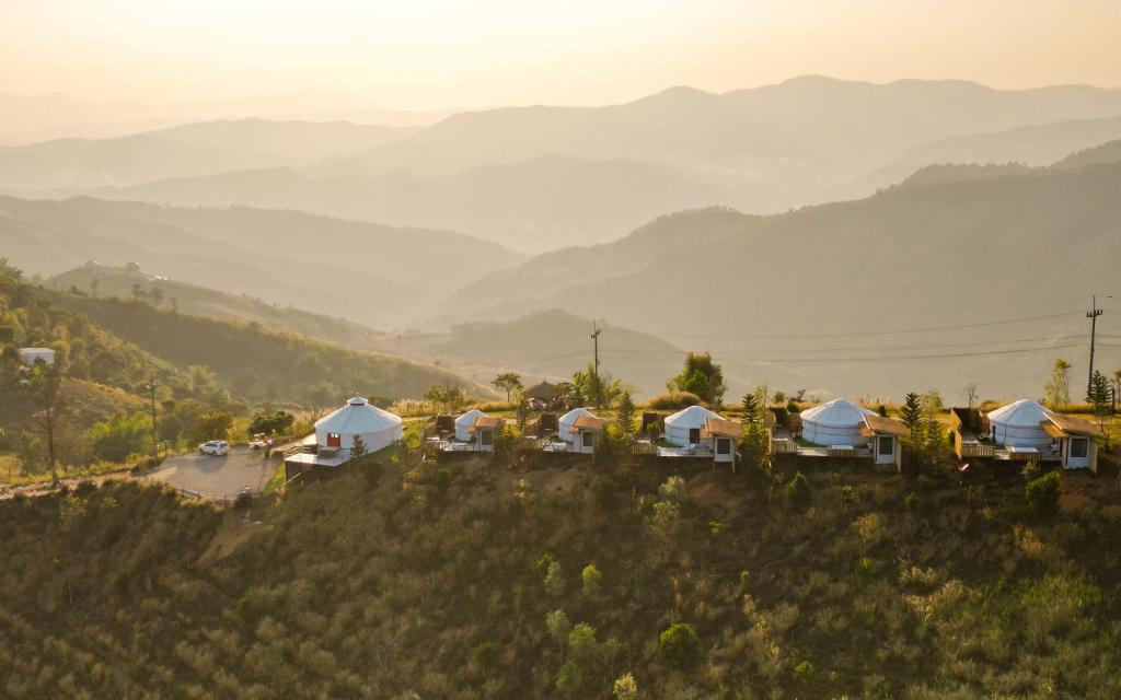 a group of tents on a hill with mountains in the background at Oasis Yurt Villa @ Doi Lan - โอเอซิส เยิร์ต วิลล่า @ ดอยล้าน in Ban Huai Khai