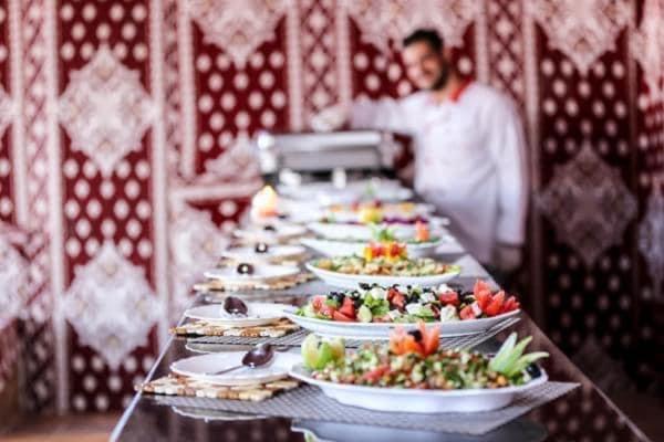 desert wadi rum camp في وادي رم: طاولة طويلة عليها أطباق من الطعام